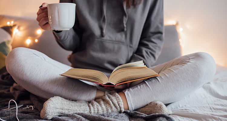 Girl drinking hot tea and reading book in bed